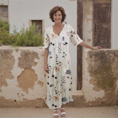 Woman in a floral dress standing against a rustic wall.