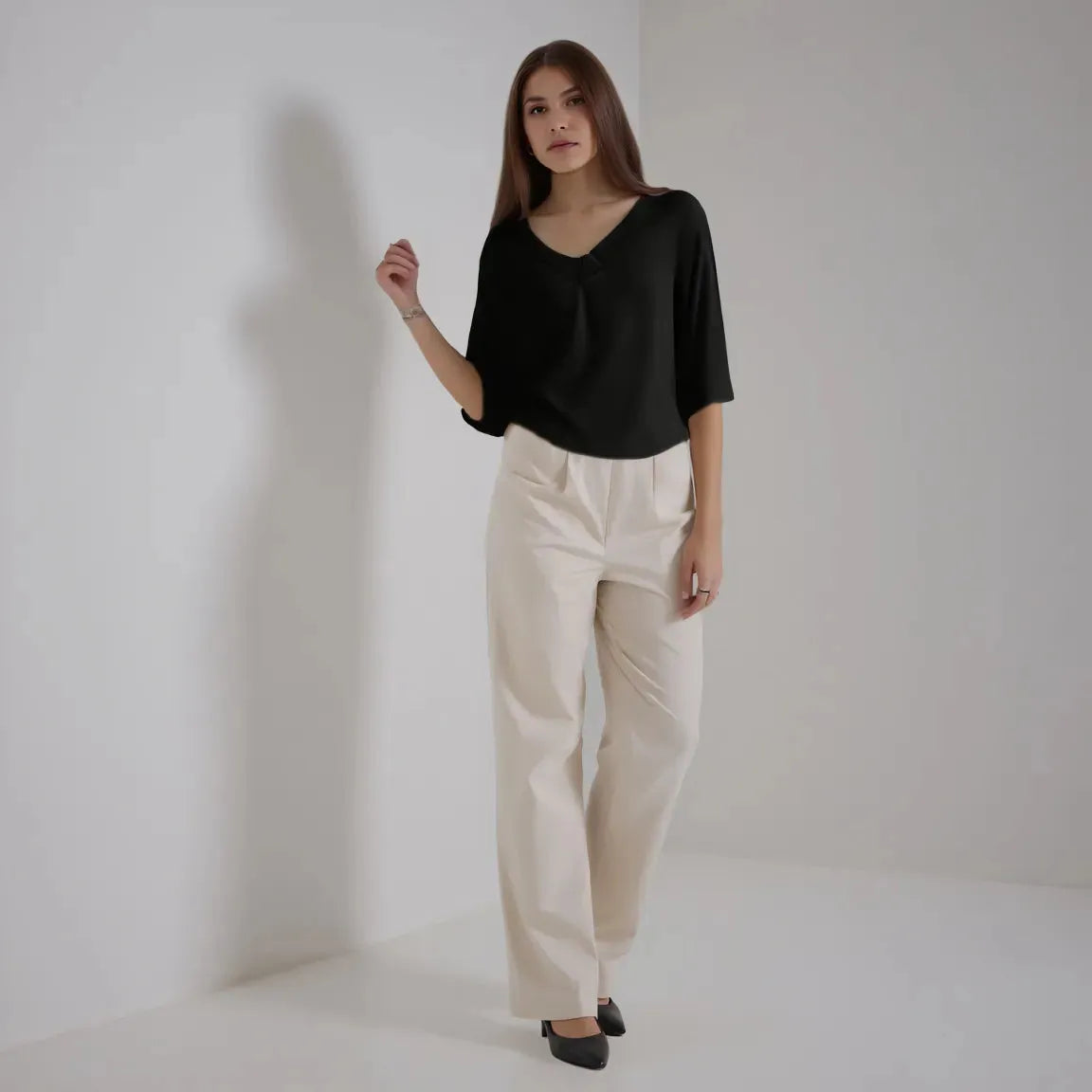 Woman wearing a black top and beige pants against a plain background