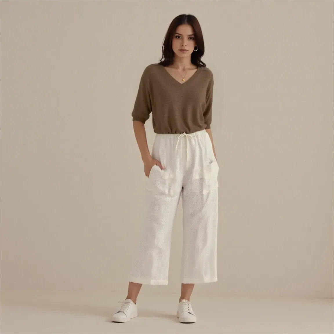 Woman wearing a brown top and white pants against a beige background