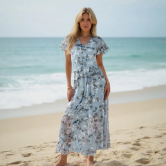 Woman in a floral dress standing on a beach with ocean in the background
