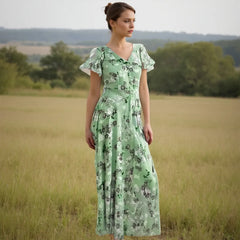 Woman in a green floral dress standing in a field with trees in the background
