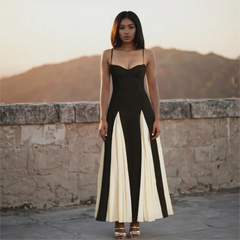 Woman wearing a black and white dress standing against a stone wall with mountains in the background