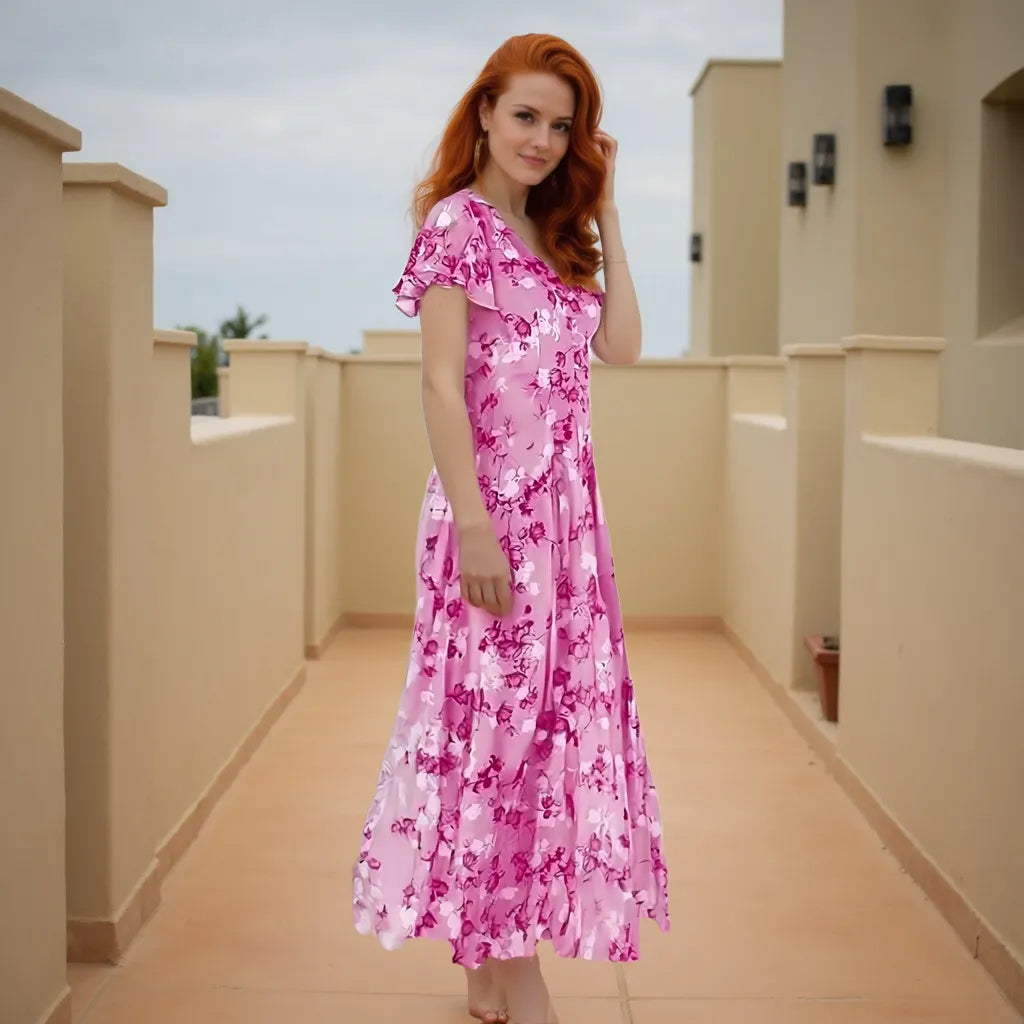 Woman in a pink floral dress standing on a rooftop with beige railings and sky in the background.
