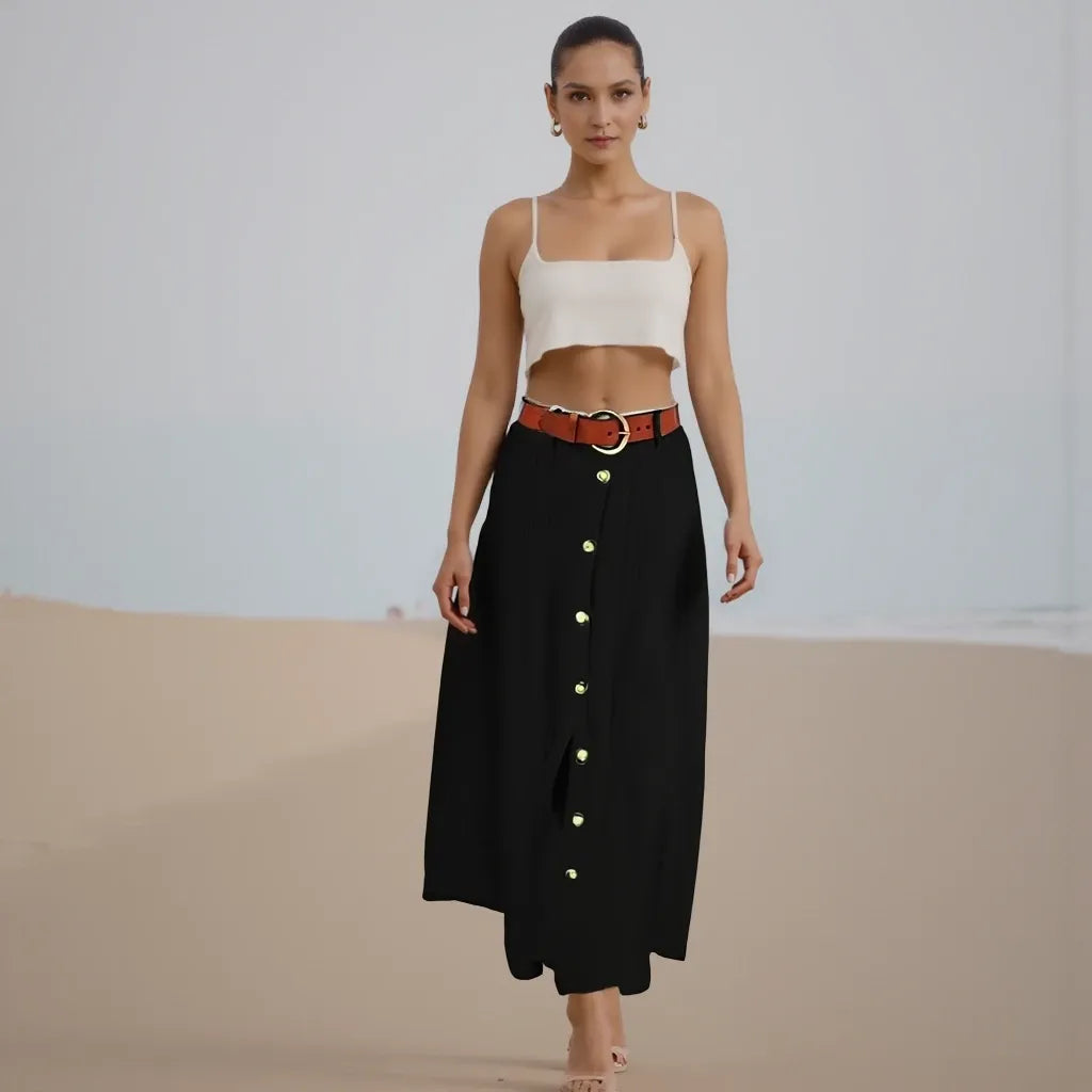 Woman wearing a white top and black skirt with gold buttons on a plain background