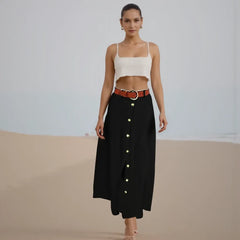 Woman wearing a white top and black skirt with gold buttons on a plain background