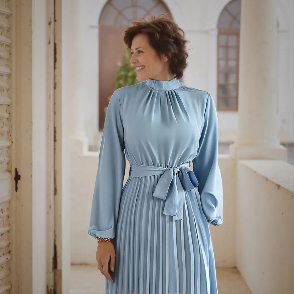 Woman wearing a light blue dress standing in an indoor setting with architectural elements.
