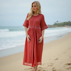 Woman in a red dress standing on a beach with ocean waves in the background
