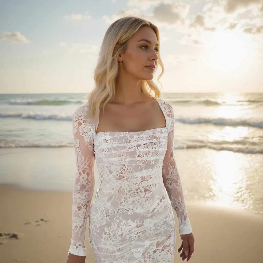 Woman in a white lace dress standing on a beach with ocean in the background