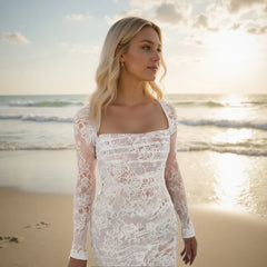 Woman in a white lace dress standing on a beach with ocean in the background