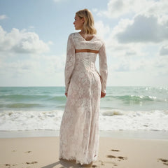 Woman in a white lace dress standing on a beach with ocean and sky in the background