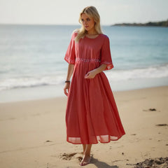 Woman in a red dress standing on a beach with ocean in the background