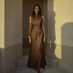 Woman in a brown dress standing in a sunlit room with shadows on the wall.