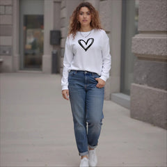 Woman wearing a white sweatshirt with a black heart design and blue jeans on a sidewalk.