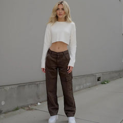 Woman wearing a white cropped sweater and brown cargo pants against a gray wall.