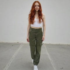 Woman wearing a white crop top and olive green cargo pants against a plain background