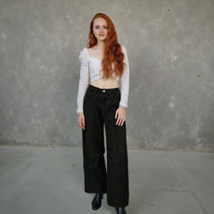 Woman wearing a white top and black pants against a gray concrete wall.