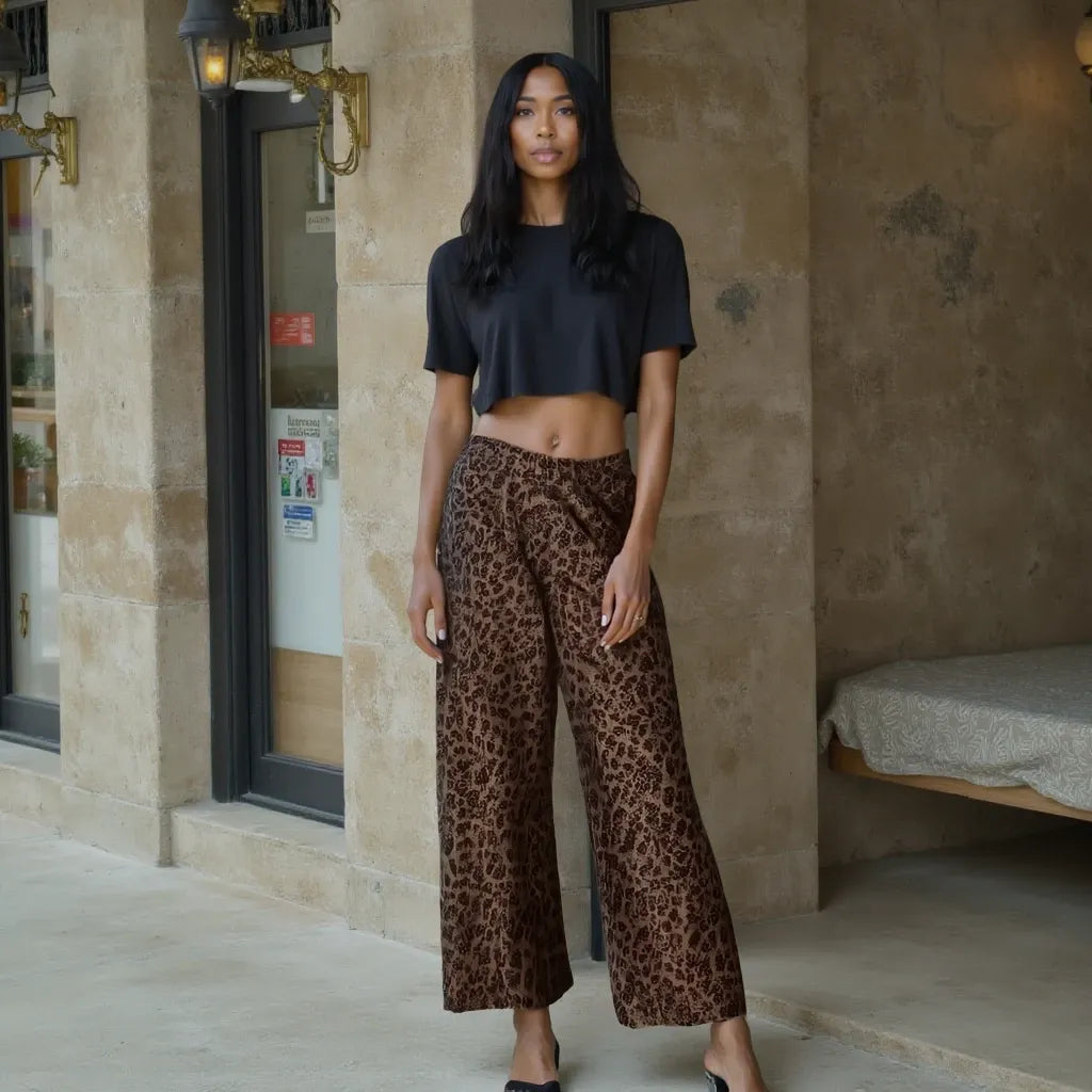 Woman wearing a black crop top and leopard print pants standing in front of a building entrance.