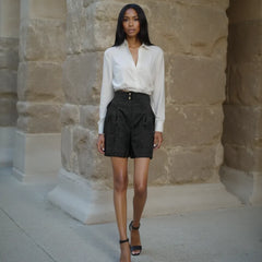Woman wearing a white blouse and black shorts standing in front of a stone wall.