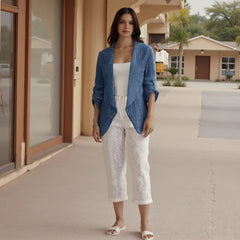 Woman wearing a blue cardigan, white top, and white lace pants standing outside a building.