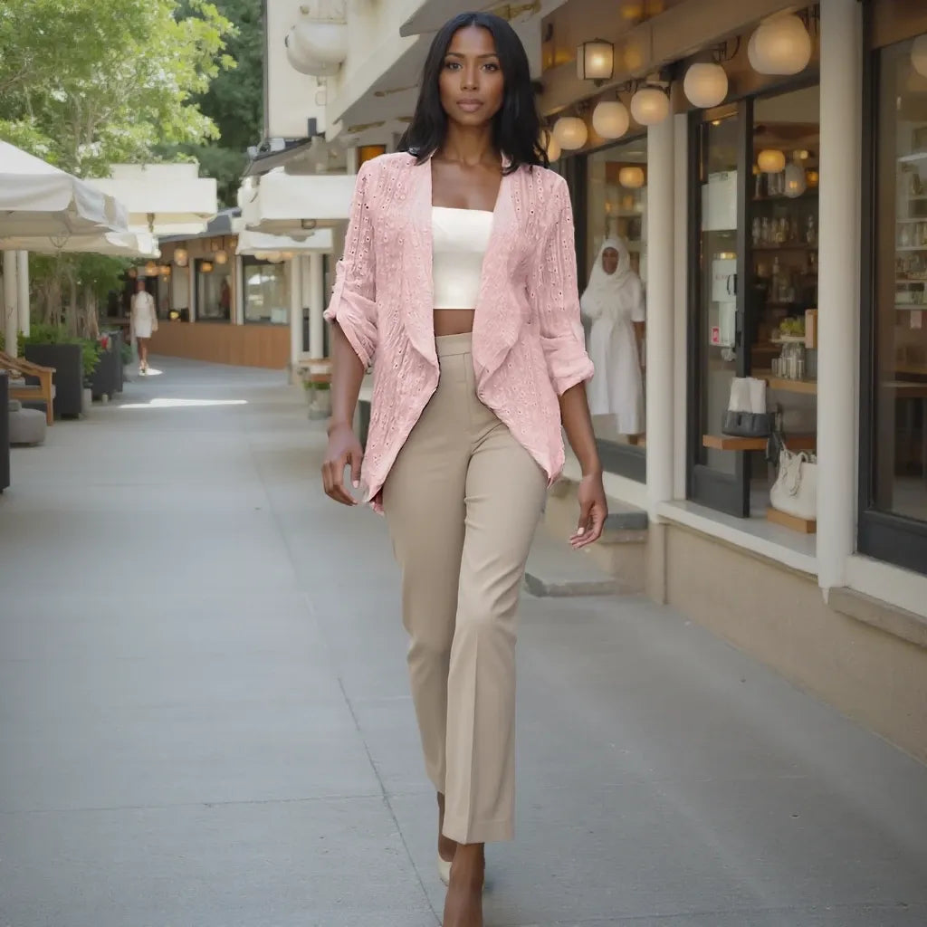 Woman in a pink cardigan and beige pants walking on a sidewalk with shops in the background.