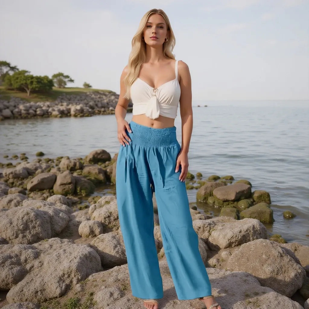 Woman in a white top and blue pants standing on rocks by a body of water.