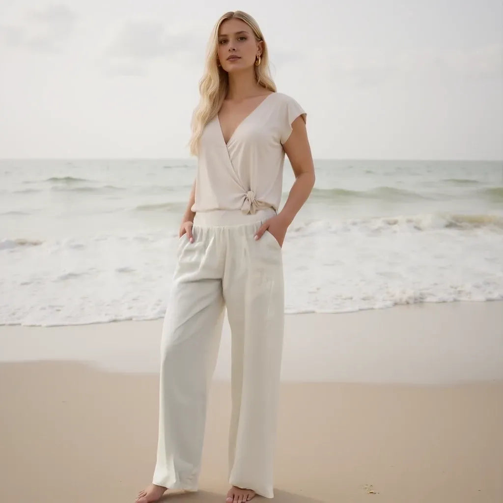 Woman in a white outfit standing on a beach with ocean in the background