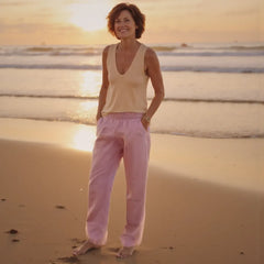 Woman standing on a beach at sunset wearing a yellow top and pink pants.