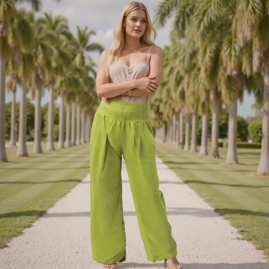 Woman in a beige top and green pants standing on a path lined with palm trees.