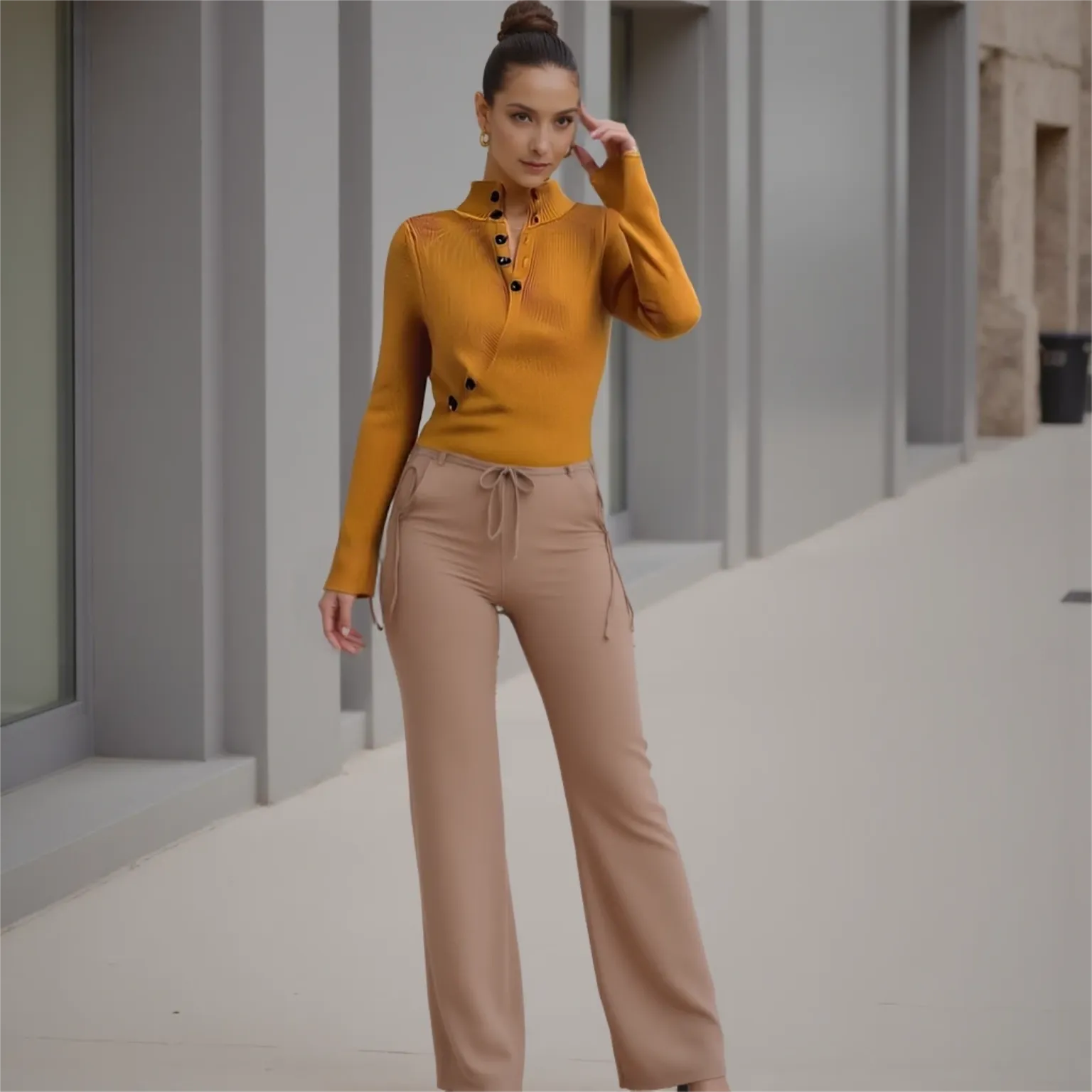 Woman wearing a mustard yellow top and beige pants standing in an urban setting.