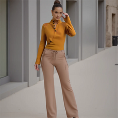 Woman wearing a mustard yellow top and beige pants standing in an urban setting.