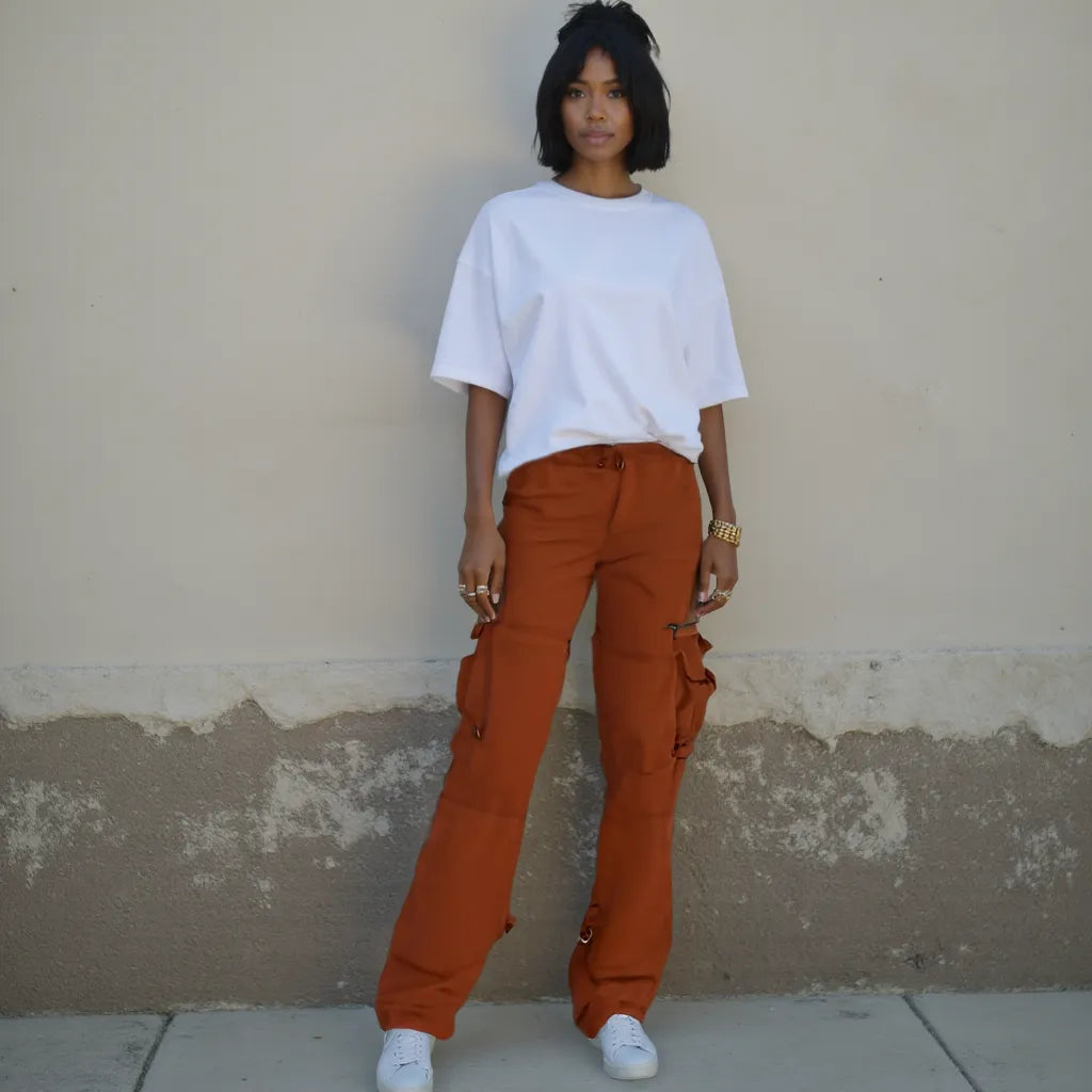 Person wearing a white shirt and orange pants standing against a beige wall.