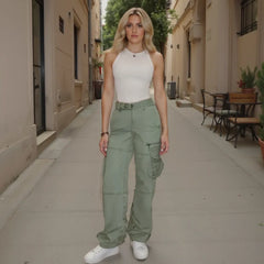 Woman wearing a white top and green cargo pants standing on a sidewalk.