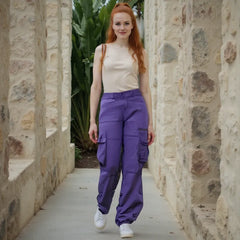 Woman wearing a beige top and purple cargo pants standing between stone walls.