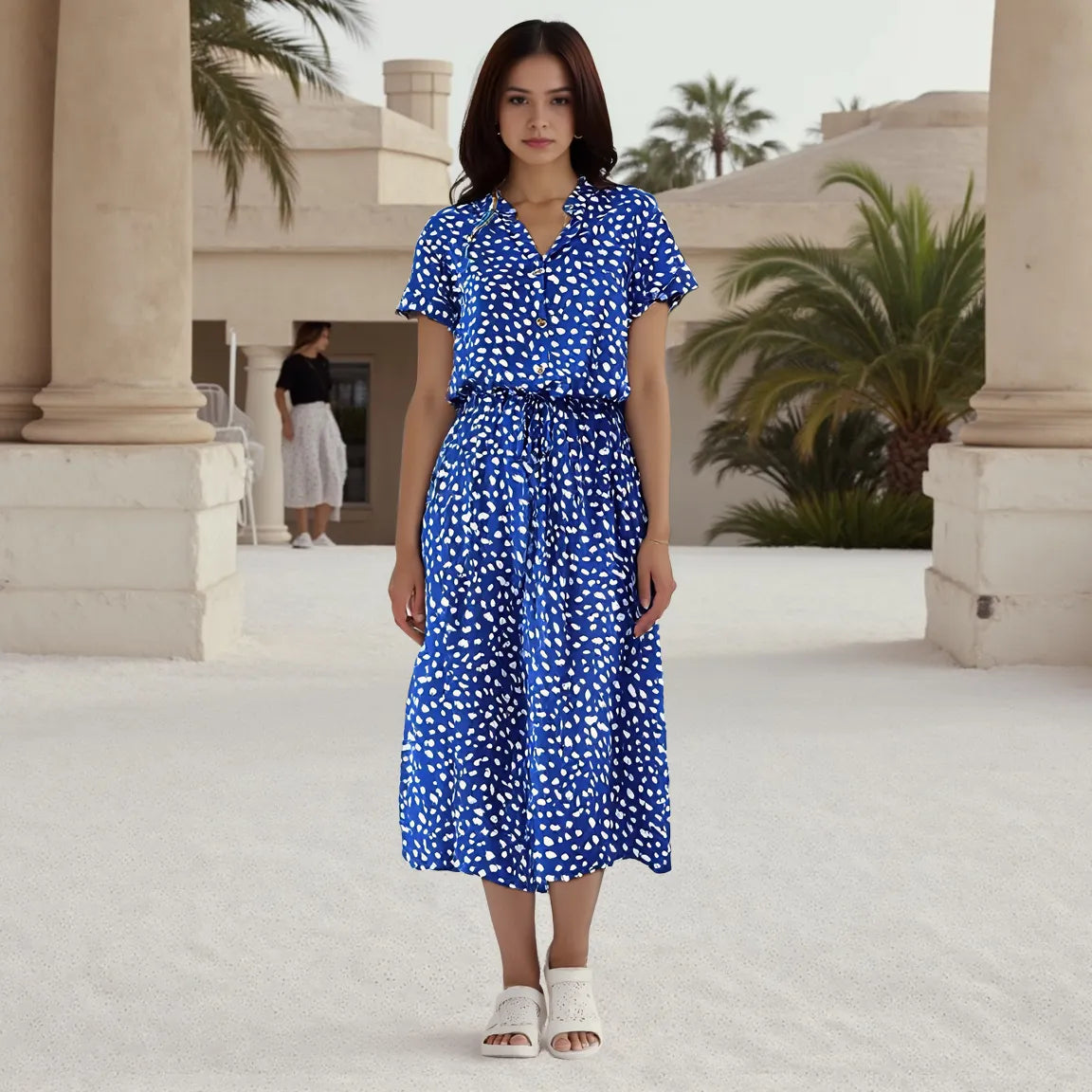 Woman wearing a blue dress with white patterns in an outdoor setting with columns and palm trees.