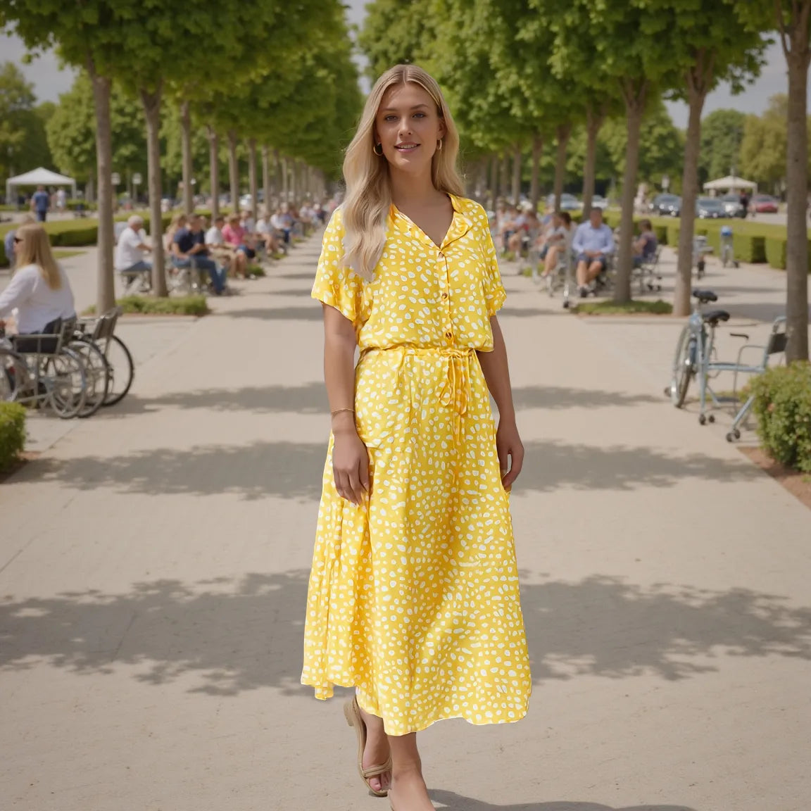 Woman in a yellow dress standing in a park with trees and people in the background