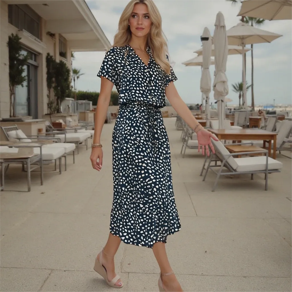 Woman in a black and white patterned dress walking outdoors near tables and chairs.