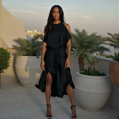 Woman in a black dress standing on a rooftop with palm trees and cityscape in the background