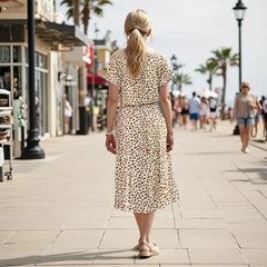 Woman in a leopard print dress walking on a city street with palm trees and people in the background.