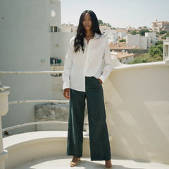 Woman in a white blouse and dark green pants standing on a rooftop with a cityscape in the background