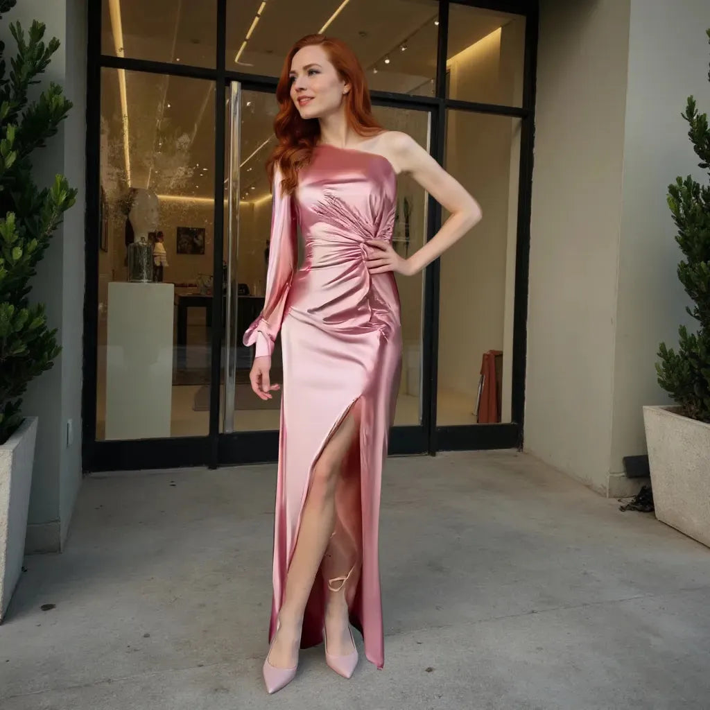 Woman in a pink satin dress standing in an indoor setting with plants and glass doors.