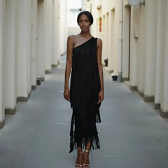 Woman wearing a black one-shoulder dress standing in a narrow alleyway.