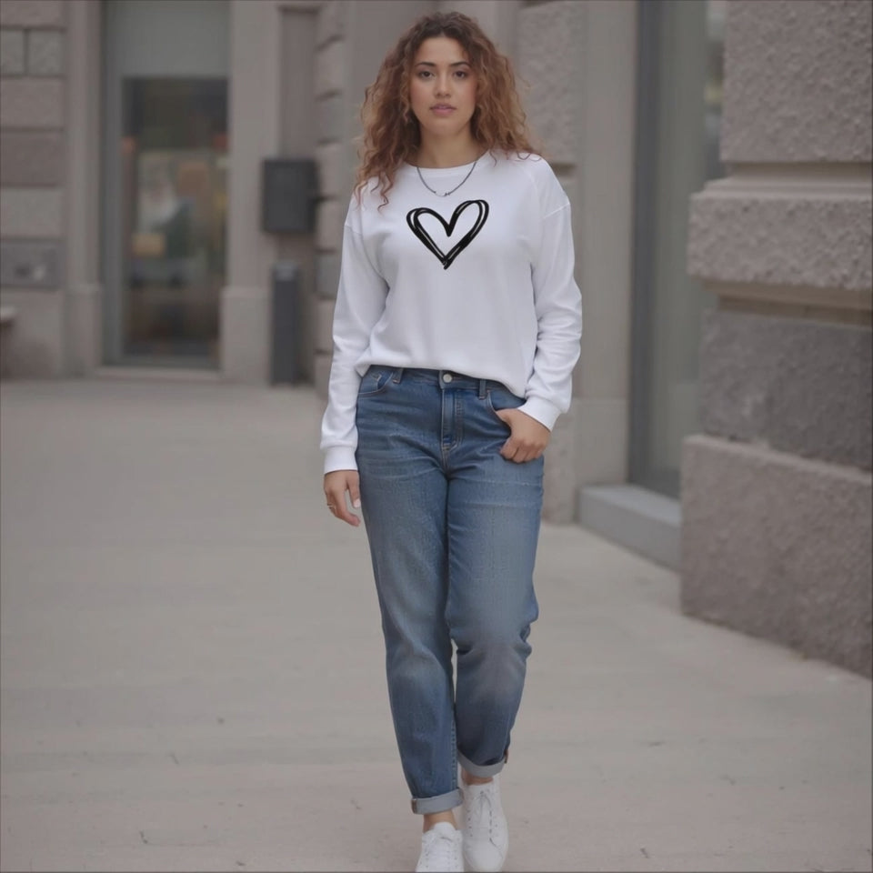 Woman wearing a white sweatshirt with a black heart design and blue jeans on a sidewalk.
