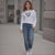 Woman wearing a white sweatshirt with a black heart design and blue jeans on a sidewalk.