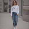 Woman wearing a white sweatshirt with a black heart design and blue jeans on a sidewalk.