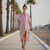 Woman in a pink dress walking on a boardwalk with palm trees in the background