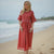 Woman in a red dress standing on a beach with ocean waves in the background