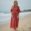 Woman in a red dress standing on a beach with ocean waves in the background