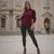 Woman wearing a burgundy hoodie and black pants standing in front of a building.