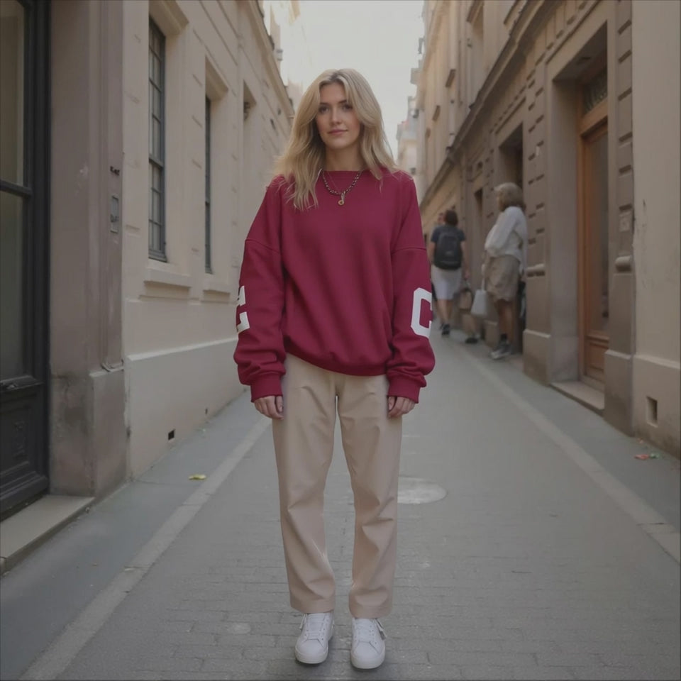 Woman wearing a red sweatshirt and beige pants standing on a city street.