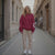 Woman wearing a red sweatshirt and beige pants standing on a city street.